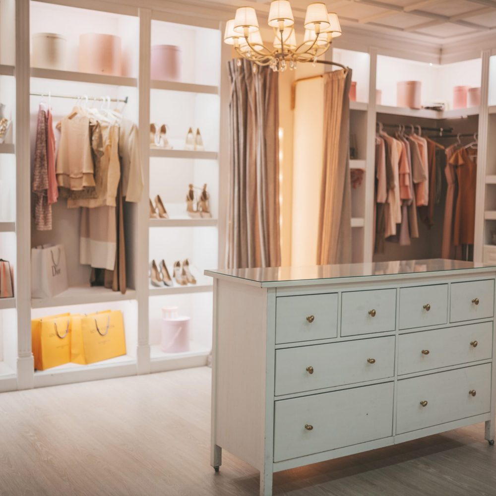 Capsule wardrobe full luxury fashion salmon colors accessories on shelves.Dressing room clothing amaranth boutique copy space table peach ecru apricot elegance dresser lavender blush modern basic wardrobe in coral puce soft-hued neutral.Feminine spring season summer style interior with white furniture big illuminated frame mirror shoe closet beige armchair pastel art mannequin heads rose tea.Pale fawn brown fashionable clothes arranged on hangers ivory outfit for fashionista Kerry Bradshaw look