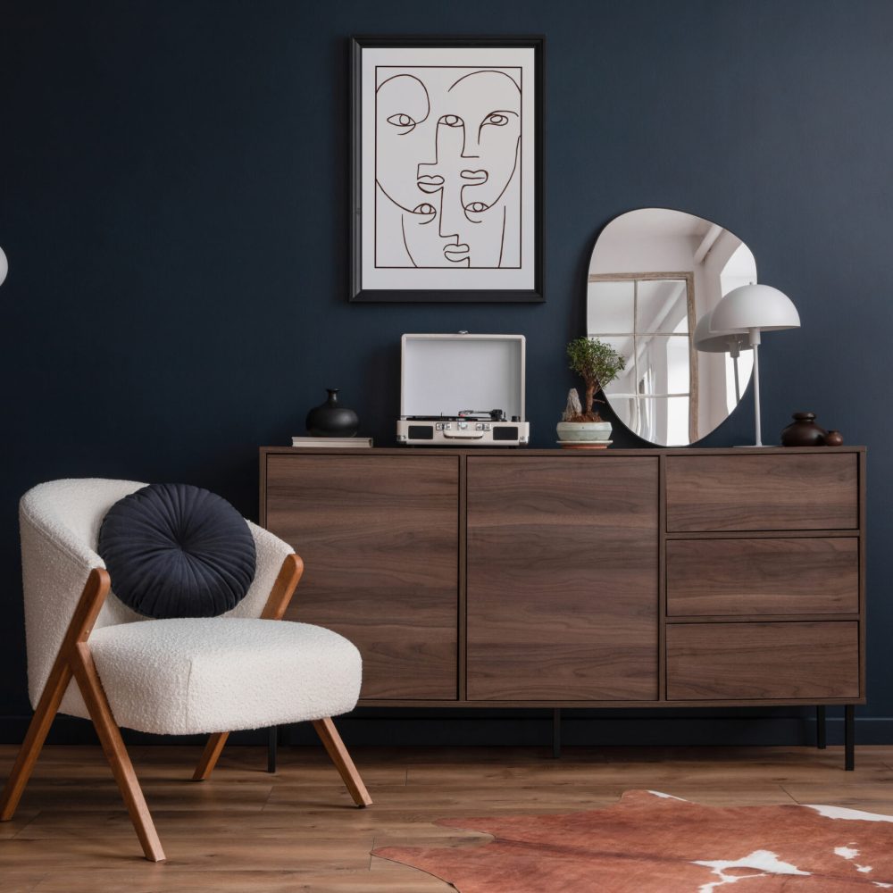 Modern living room interior composition with fluffy armchair, wooden commode, mock up poster frame, vinyl recorder and modern home accessories. Blue wall. Template. Copy space.